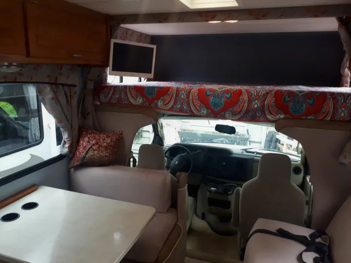 RV rental interior with a cozy dining area, an overhead cab bed with patterned bedding, and the driver's cabin.. Other Other 2009