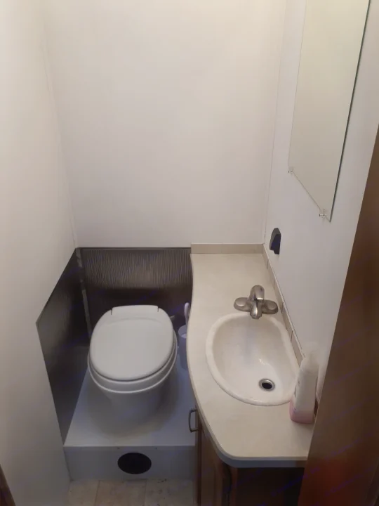 Compact RV rental bathroom with a toilet on a raised base, sink, counter, and mirror. Features white walls and dark lower paneling.. Other Other 2009