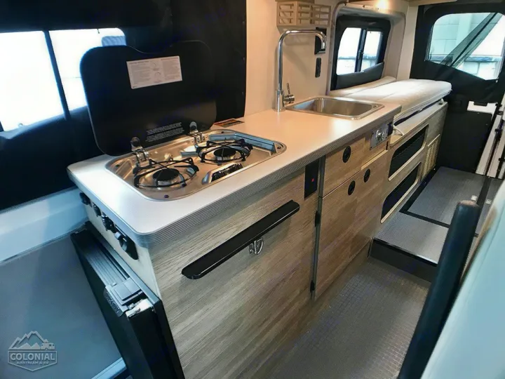 This RV rental's campervan interior features a modern kitchenette with a two-burner stove, sink, and ample storage, beside a bed.. Winnebago Solis 2021