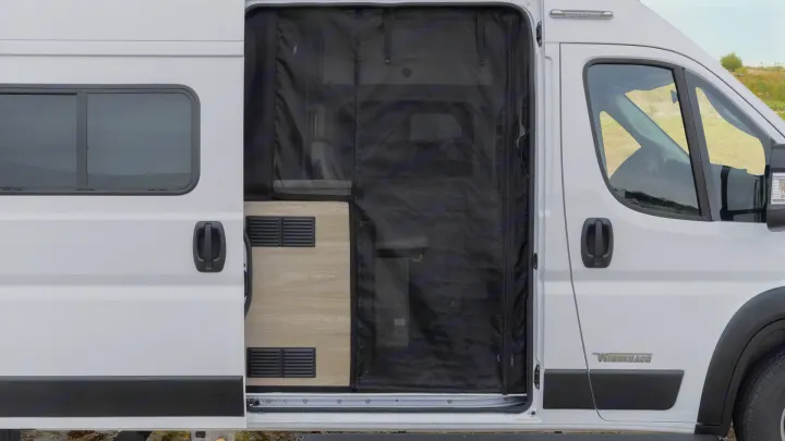 Side of a white RV rental camper van with sliding door open, showing a black screen door and interior with wood-look floor.. Winnebago Solis 2021