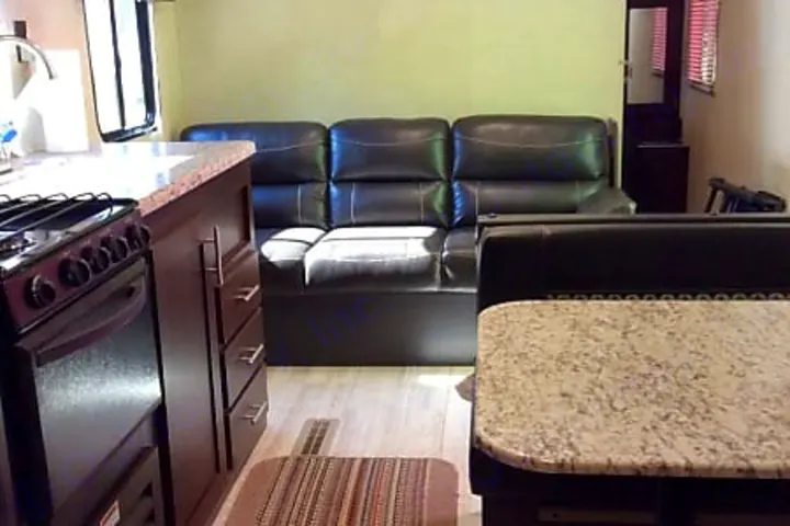 Spacious RV rental interior featuring a kitchen area, a comfortable dark sofa, and a dining booth.. kz 26' SPORTSMAN 2018