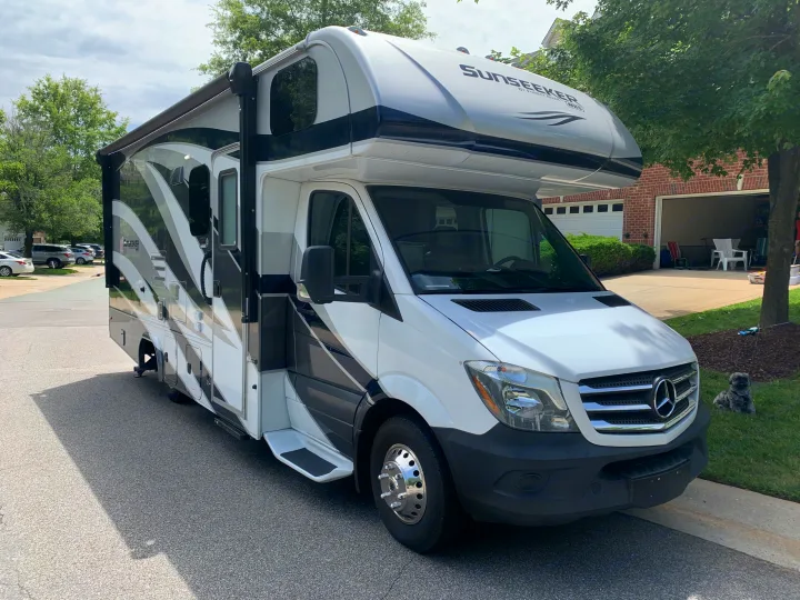 Sunseeker Class C RV rental, white and black, parked on a residential street. A small dog rests in the grass nearby.. Forest River Sunseeker 2019