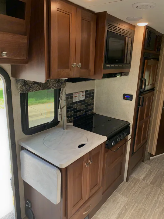 Modern RV rental kitchen with sink, stove, microwave, fridge, and pull-out counter for efficient compact living.. Forest River Sunseeker 2019