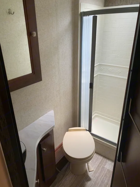 Inside a functional RV rental bathroom with a toilet, stand-up shower, and vanity with sink and mirror.. Forest River Sunseeker 2019
