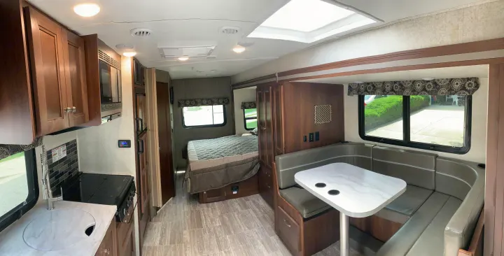 This spacious RV rental interior features a kitchen, bed, and U-shaped dinette, offering comfort for travel adventures.. Forest River Sunseeker 2019