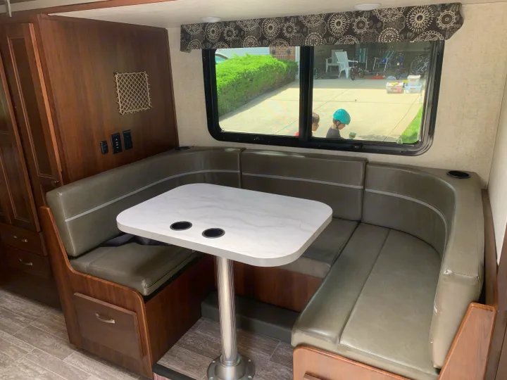 Spacious RV rental dinette with comfortable U-shaped seating, table with cupholders, and large window view.. Forest River Sunseeker 2019