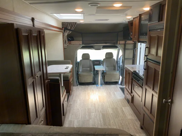 Spacious RV rental interior: kitchen, dining booth, overhead bunk, and cab area with dark wood cabinets and light flooring.. Forest River Sunseeker 2019