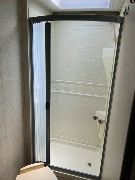 This clean, compact RV shower, featuring a curved door and white subway tile-look walls, is ready for your rv rental trip.. Forest River Sunseeker 2019