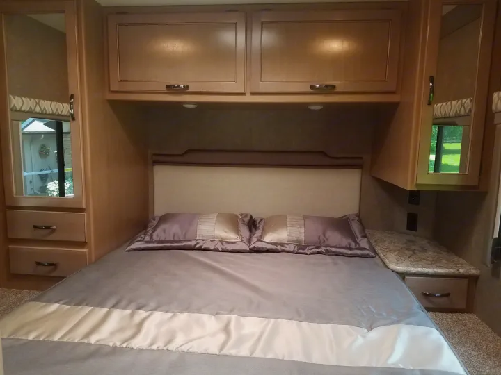 Cozy RV rental bedroom featuring a comfortable bed, overhead cabinets, and built-in storage on both sides.. Thor Four Winds 2020