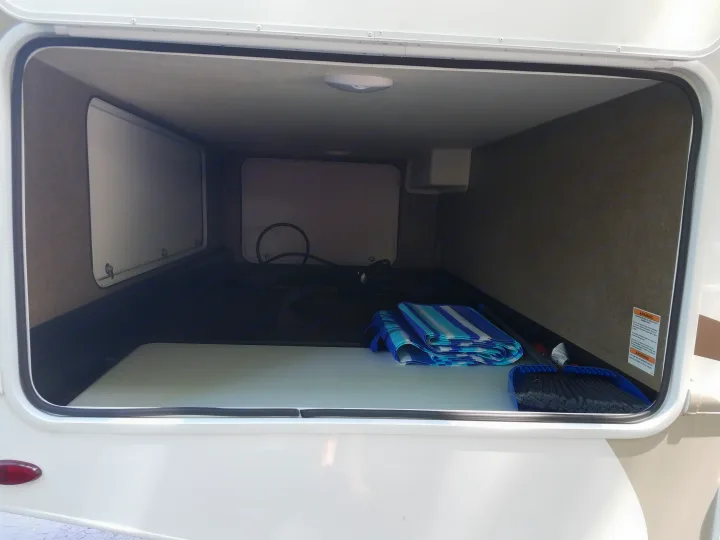 Spacious RV rental pass-through storage bay, clean and ready for gear. Interior shows hose, mat, and broom.. Thor Four Winds 2020
