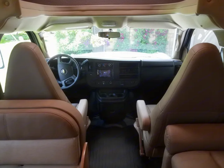Inside an RV rental, the front cabin reveals the dashboard, steering wheel, and two tan driver/passenger seats with a clear view outside.. Thor Four Winds 2020