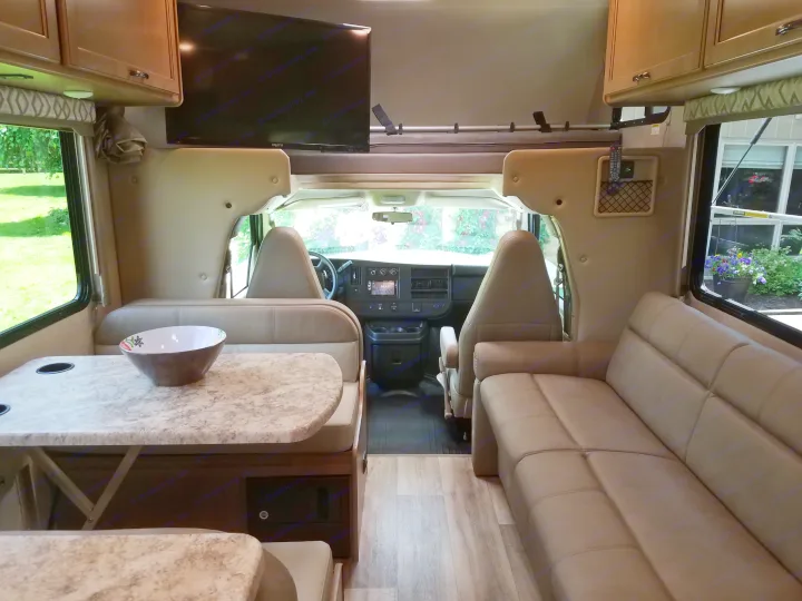An RV rental interior with a comfy sofa, dining area, overhead storage, TV, and a view into the driver's cabin.. Thor Four Winds 2020