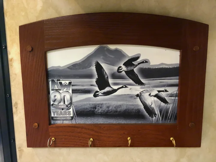 RV rental wall decor: A wooden frame with key hooks features a black and white image of flying geese and the Northwood logo.. Northwood Mfg Nash 2014