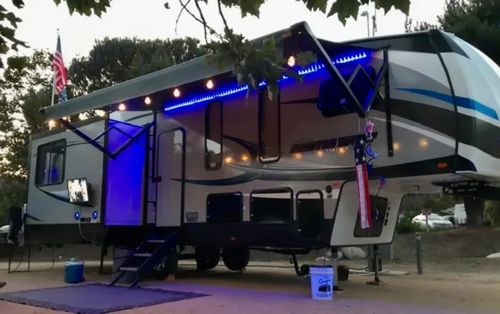 Enjoying an evening in a spacious RV rental. Illuminated awning, outdoor TV, and festive decorations visible.. Forest River Cherokee Wolf Pack 2019