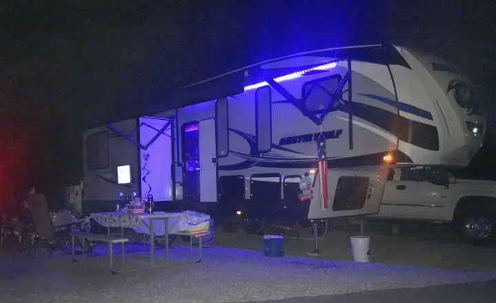 Nighttime rv rental setup: a large camper with blue LED lights, picnic area, and truck at a dark campsite.. Forest River Cherokee Wolf Pack 2019