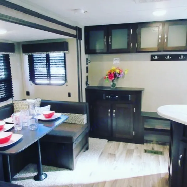 This RV rental features a comfortable dining booth, dark wood cabinets, and bright flowers, creating a cozy interior space.. Keystone Springdale 2020