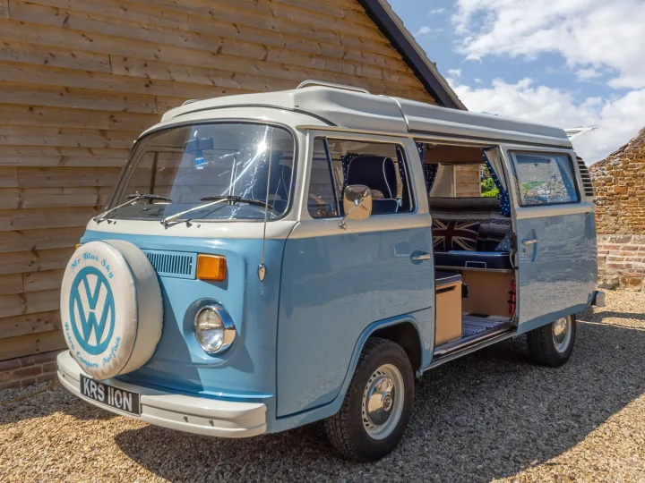 This classic blue & white VW camper van, an inviting rv rental, has its side door open revealing a cozy interior for adventure.. Volkswagen 2.0L T2 Late Bay 1975