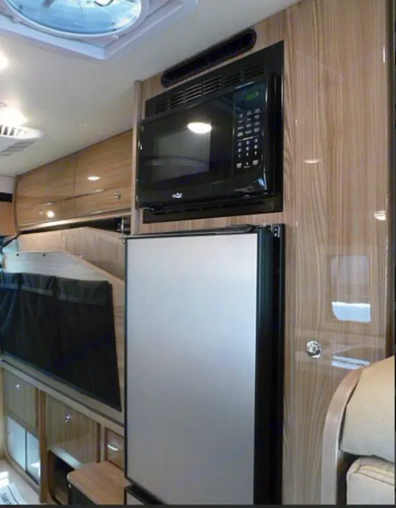 RV rental interior: Ceiling vent, built-in microwave, fridge, and stylish wood cabinets for compact living on the road.. Winnebago Travato 2020