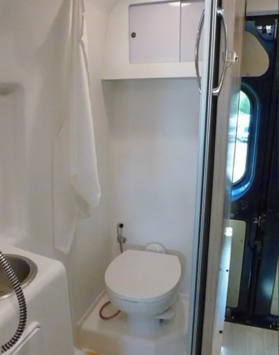 Compact RV rental bathroom: a white toilet, sink with shower sprayer, and curtain maximize space.. Winnebago Travato 2020