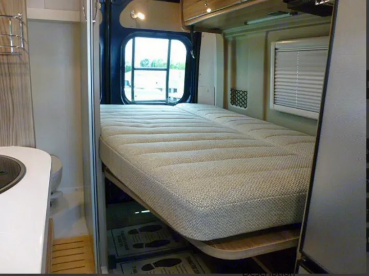 Inside an RV rental: a versatile, elevated bed, compact kitchen counter, and bathroom optimize the small living space.. Winnebago Travato 2020