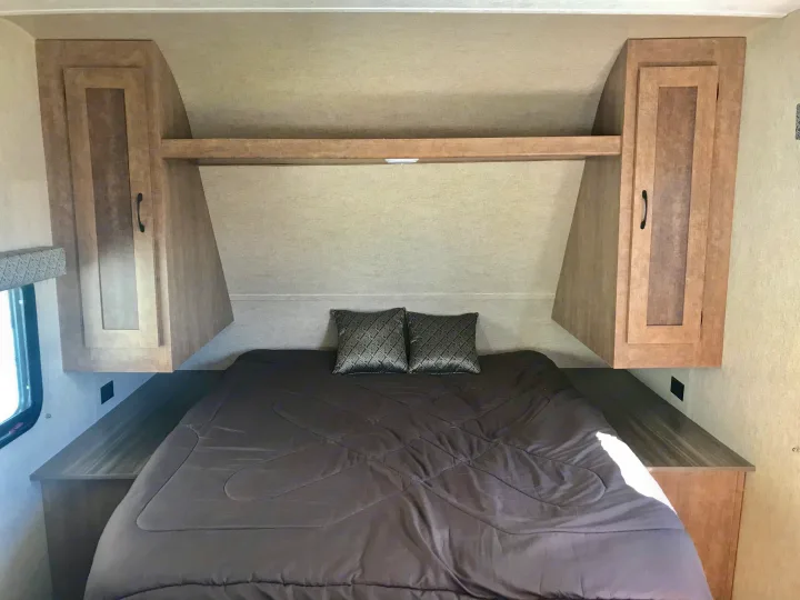 RV rental bedroom with a full-sized bed, dark comforter, patterned pillows, overhead cabinets, and side storage.. Starcraft Ar-One 2017