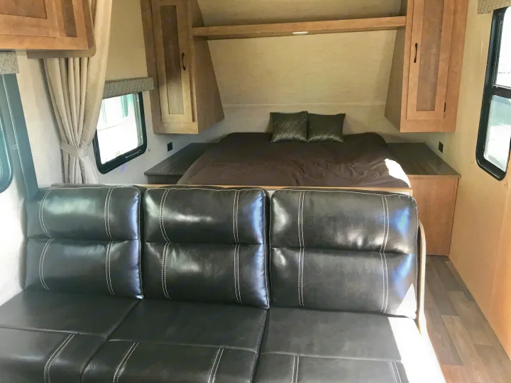 Cozy RV rental interior featuring a bed with overhead cabinets, side tables, and a comfortable black leather sofa.. Starcraft Ar-One 2017