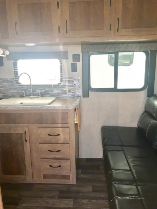 This RV rental features a compact kitchen with a sink, cabinets, and a stylish black sofa in the adjacent dining/lounge area.. Starcraft Ar-One 2017