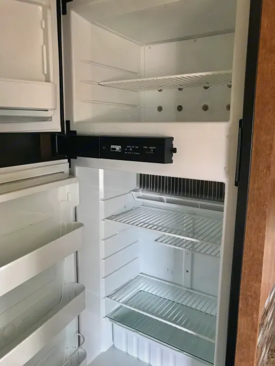 Open, empty RV rental refrigerator, featuring clean white shelves and a Norcold control panel for temperature settings.. Starcraft Ar-One 2017