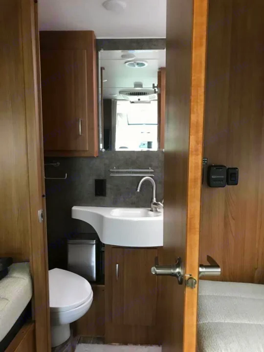 Inside an RV rental: compact bathroom with toilet, sink, mirror, and light wood interior. Ideal for road trips.. Winnebago Trend 2017