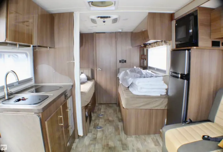 Tour this RV rental interior: compact kitchen with sink/stovetop, two beds with bedding, refrigerator, & microwave setup.. Winnebago Trend 2017