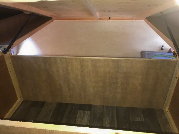 View inside an RV rental's under-bed storage, featuring a dark laminate floor, light paneling, and gas lift supports.. Starcraft Ar-One 2017