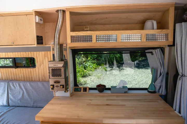 Cozy RV rental interior with wooden built-ins, Dickinson heater, and large window. Perfect for van life adventures.. RAM Promaster 1500 2017