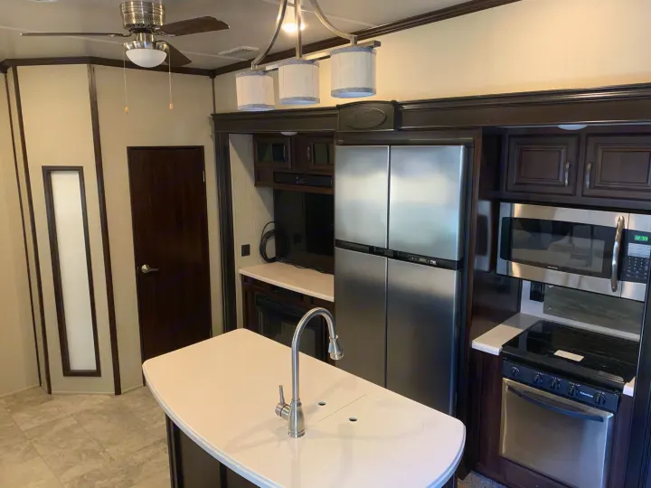 Spacious RV rental kitchen & living area features modern stainless appliances, island, and dark wood trim.. Palomino Columbus 2018