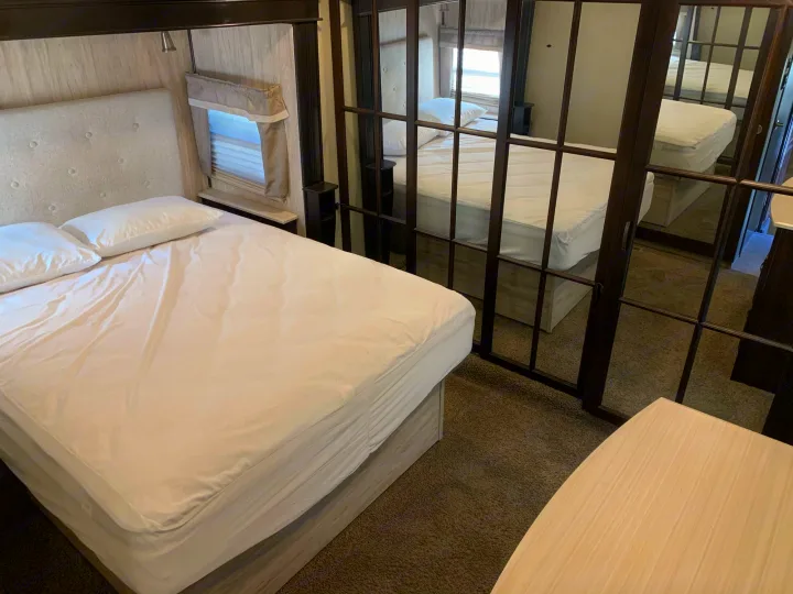 Bright RV rental bedroom showcasing a clean, comfortable bed with white linens, a window, and mirrored closet doors.. Palomino Columbus 2018