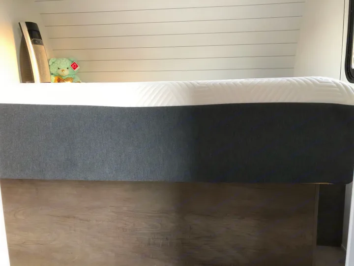 Inside an RV rental: a cozy bed with a dark base, white top, shiplap walls, and a small teddy bear on the shelf.. Forest River EVO 2020