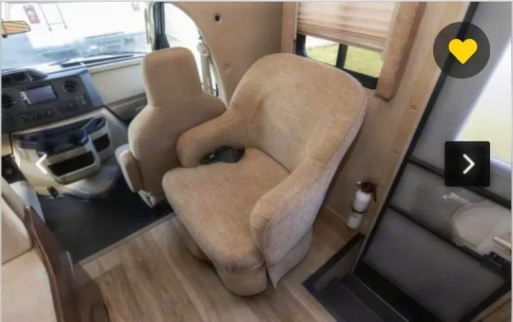 Spacious RV rental interior featuring a comfy armchair, front cabin seats, and sleek wooden floors.. Thor Freedom Elite 2018