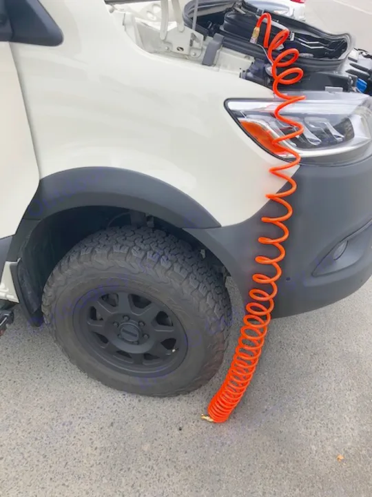Orange air hose connecting to an RV rental tire, likely for inflation. Prepping for travel.. Winnebago Revel 2020