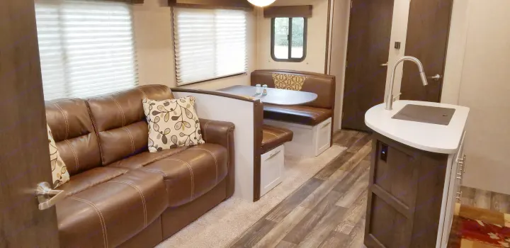 RV rental living space featuring a leather sofa, dinette booth, and a compact kitchen counter.. Other Other 2019
