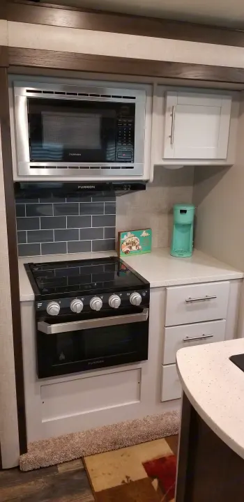 Interior view of an RV rental kitchen showing Furrion microwave, range, oven, white cabinets,. Other Other 2019