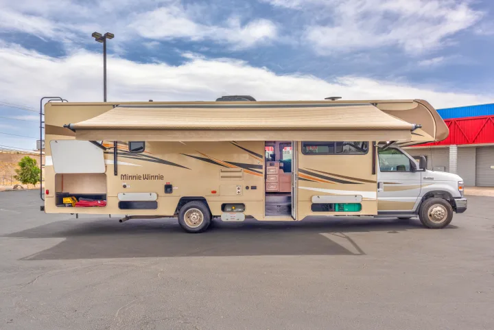 Minnie Winnie RV rental: A beige motorhome with an extended awning, open storage compartments, and entry door, parked on asphalt.. Winnebago Winnebago 2019