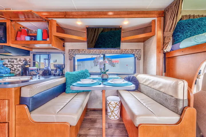 Experience a bright RV rental interior featuring a full kitchenette, comfy dinette with teal decor, TV, and bunk bed for travelers.. Winnebago Winnebago 2019