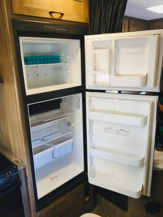 Open RV rental refrigerator/freezer unit, showing clean interior with shelves & bins, ready for your travels.. Coachmen Prism 2016