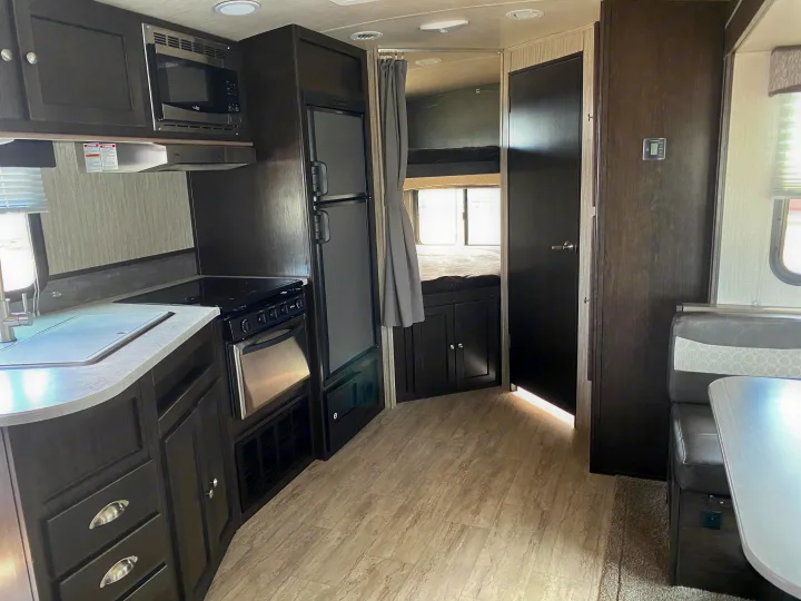 Inside a stylish rv rental: dark wood kitchen with stove, microwave, fridge, and a glimpse of cozy bunk beds.. Cruiser RV Shadow Cruiser 2019