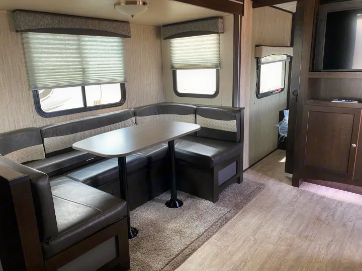 Spacious RV rental living area featuring a dark U-shaped dinette with a table, large windows, and a TV.. Cruiser RV Shadow Cruiser 2019