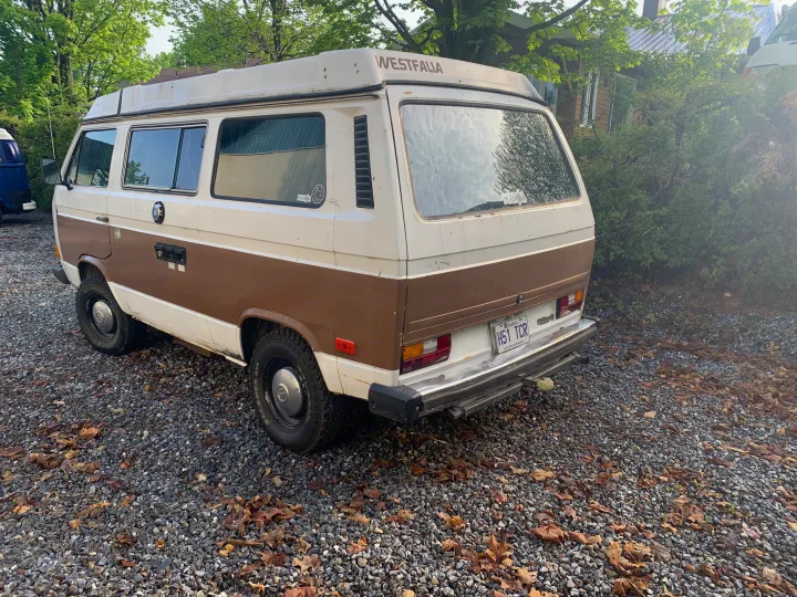 A classic brown and white Volkswagen Westfalia camper van on a gravel lot. Ideal for an rv rental road trip or outdoor adventure.. Volkswagen T3 Westfalia 1984