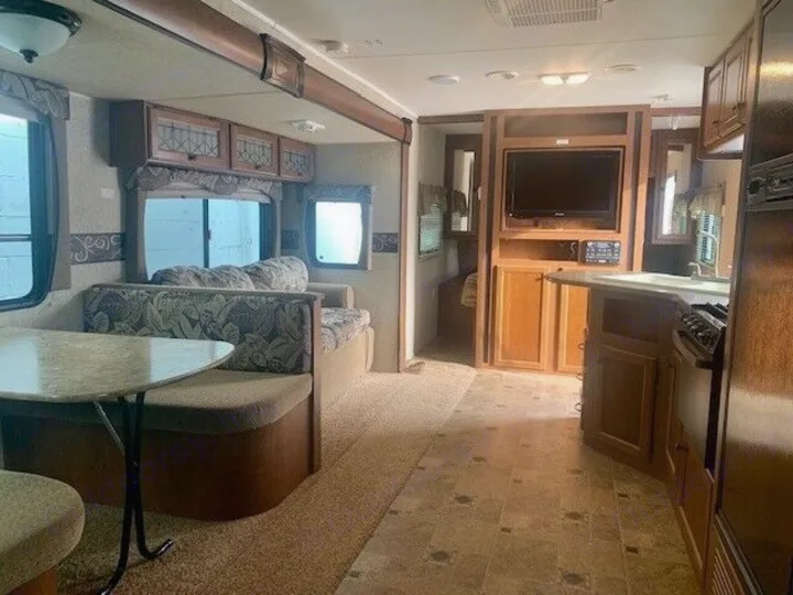 Spacious RV rental interior featuring a cozy dining nook, living area with sofa, and a functional kitchen with stove and sink.. Heartland Prowler 2012