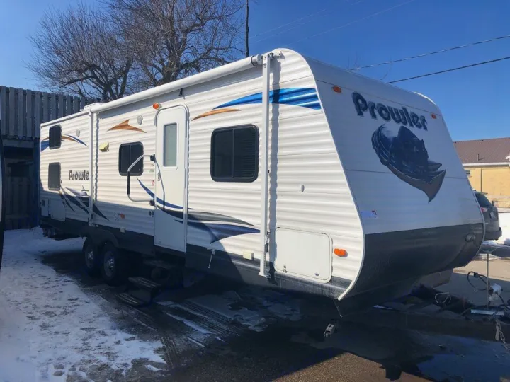 White Prowler travel trailer RV with blue/brown stripes and a wolf graphic on the front, parked on melting snow. Great rv rental.. Heartland Prowler 2012