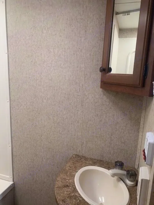 Compact RV rental bathroom features a sink, faucet, wood medicine cabinet, and textured walls.. Heartland Prowler 2012