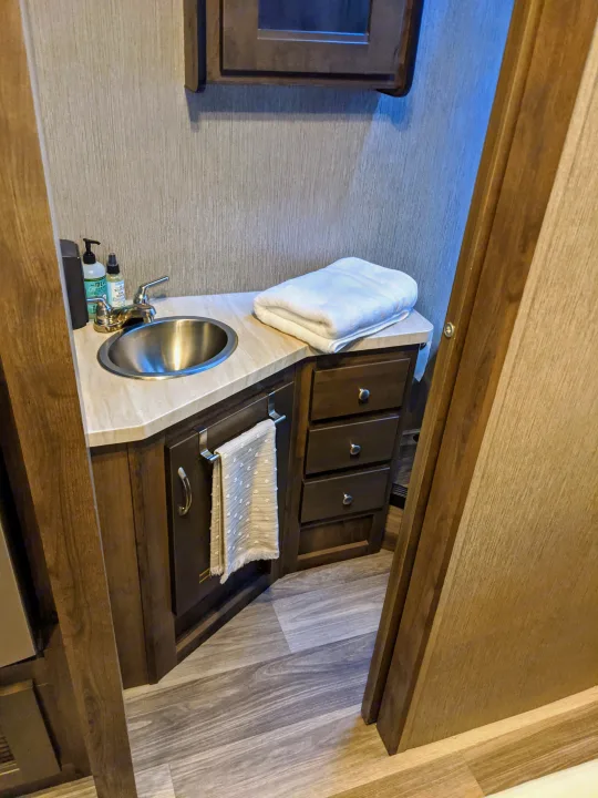 Compact RV rental bathroom with a stainless steel sink, wood vanity, and fresh towels for your comfort.. Nexus RV Triumph 2020