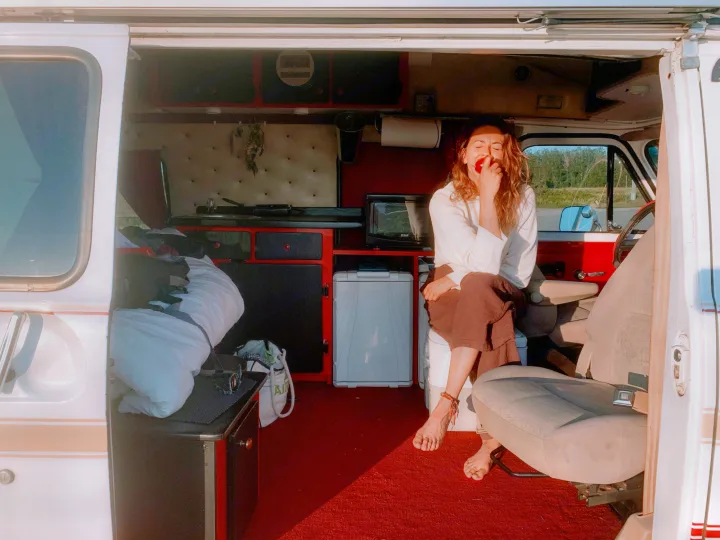 Embrace the journey! A woman unwinds barefoot in a cozy RV rental camper, enjoying van life amidst red interiors and sunlight.. Chevrolet G20 1983